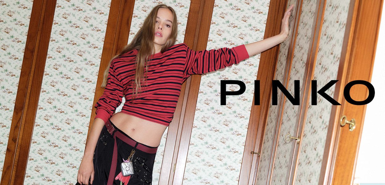 Top corto a rayas rojas y negras, con manga larga y escote amplio, combinado con pantalones negros adornados con acentos y detalles decorativos.