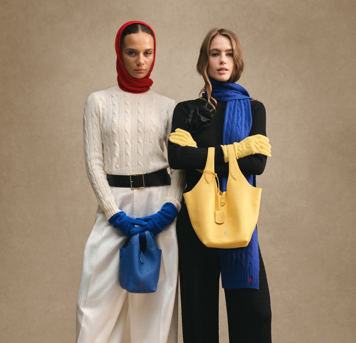 Due donne indossano abbigliamento invernale e accessori colorati. La prima indossa un maglione in lana color crema a trecce, una sciarpa rossa, guanti blu e tiene in mano una borsa blu. La seconda indossa un completo nero, una sciarpa blu, guanti gialli e porta una borsa gialla.