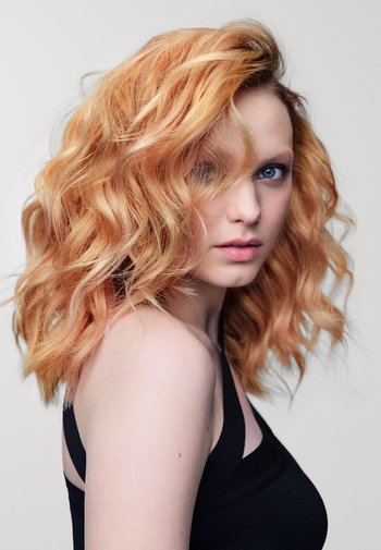 Wavy, shoulder-length hair in a light orange shade, with a smooth texture. The subject wears a black, sleeveless top with thin straps.