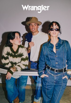 Tre personer poserer sammen, iført en grønn og hvit stripete genser, et denim jumpsuit og en hvit skjorte, med en nøytral bakgrunn.