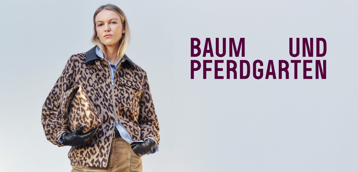 Leopard print jacket with a zip front, black collar, and side pockets; worn over a light blue shirt and paired with a matching patterned bag.