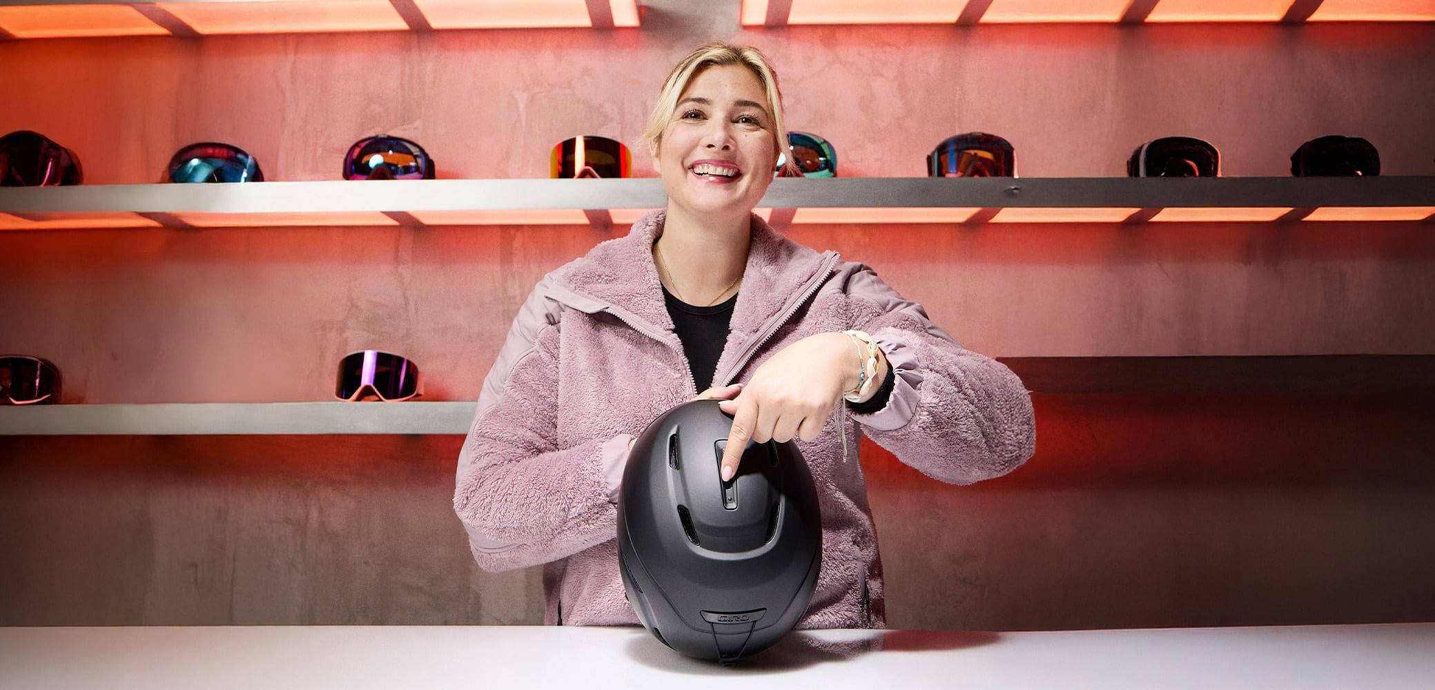 Schwarzer Skihelm mit verstellbarer Funktion; glatte, abgerundete Form. Der Hintergrund zeigt mehrere Skibrillen. Warmes Licht verbessert die Sichtbarkeit.