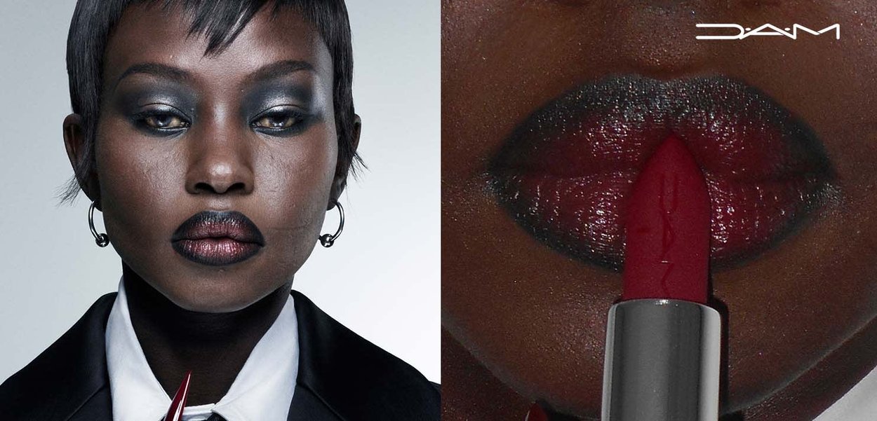 Röd läppstift med glansig finish hålls nära mörka, väldefinierade läppar. Modellen har kort mörkt hår och bär en svart kavaj.