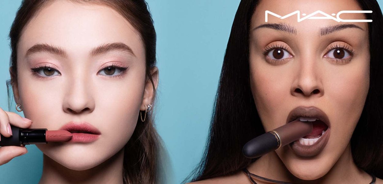 Deux femmes appliquent du rouge à lèvres : l'une tient une teinte rose pâle près de ses lèvres, l'autre a un rouge à lèvres brun foncé dans la bouche, avec le logo MAC au-dessus.