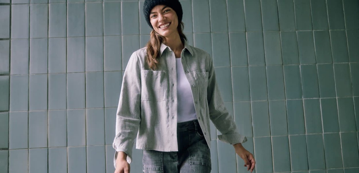 Graue Jacke mit Knöpfen und zwei Taschen, getragen über einem weißen Hemd und dunkelblauer Jeans, ergänzt durch eine schwarze Strickmütze. Strukturierter Stoff.