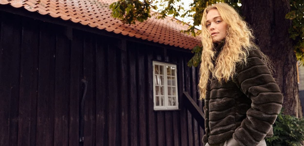 Tekoturkistakki vaakasuorilla raidoilla tummassa värissä, jossa on korkea kaulus ja rento istuvuus, yhdistettynä vaaleisiin housuihin.