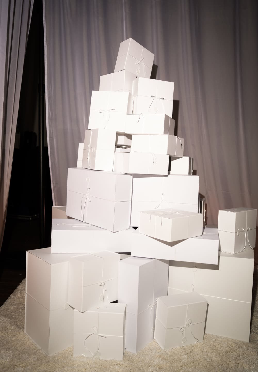 Hög med olika vita lådor med rosettband, i varierande storlekar och former, staplade i en pyramid på en ljus yta.