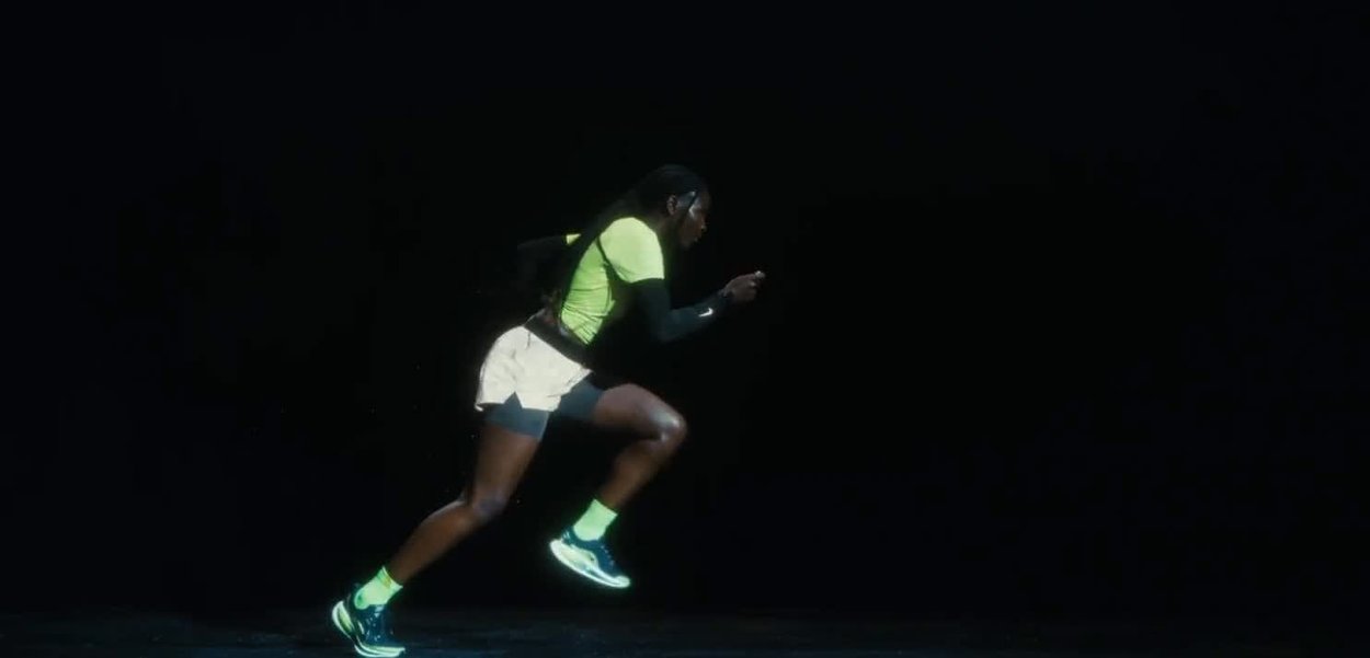 Ropa deportiva que incluye una camiseta de manga corta en un brillante verde neón, mangas largas negras y pantalones cortos claros, junto con zapatillas de correr y calcetines.