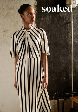 Abito a righe bianche e nere con collo alto e maniche corte. Presenta un dettaglio annodato al colletto e una silhouette fluida.