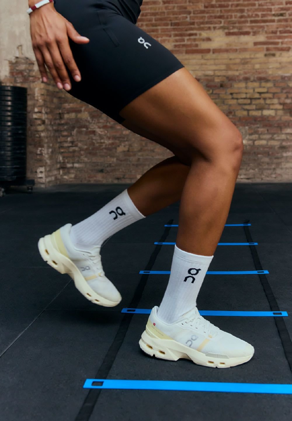 Weiße Sportschuhe mit auffälliger Markenkennzeichnung, strukturierten Sohlen und gepolstertem Design, getragen mit weißen Socken mit Logo, auf schwarzem Boden.