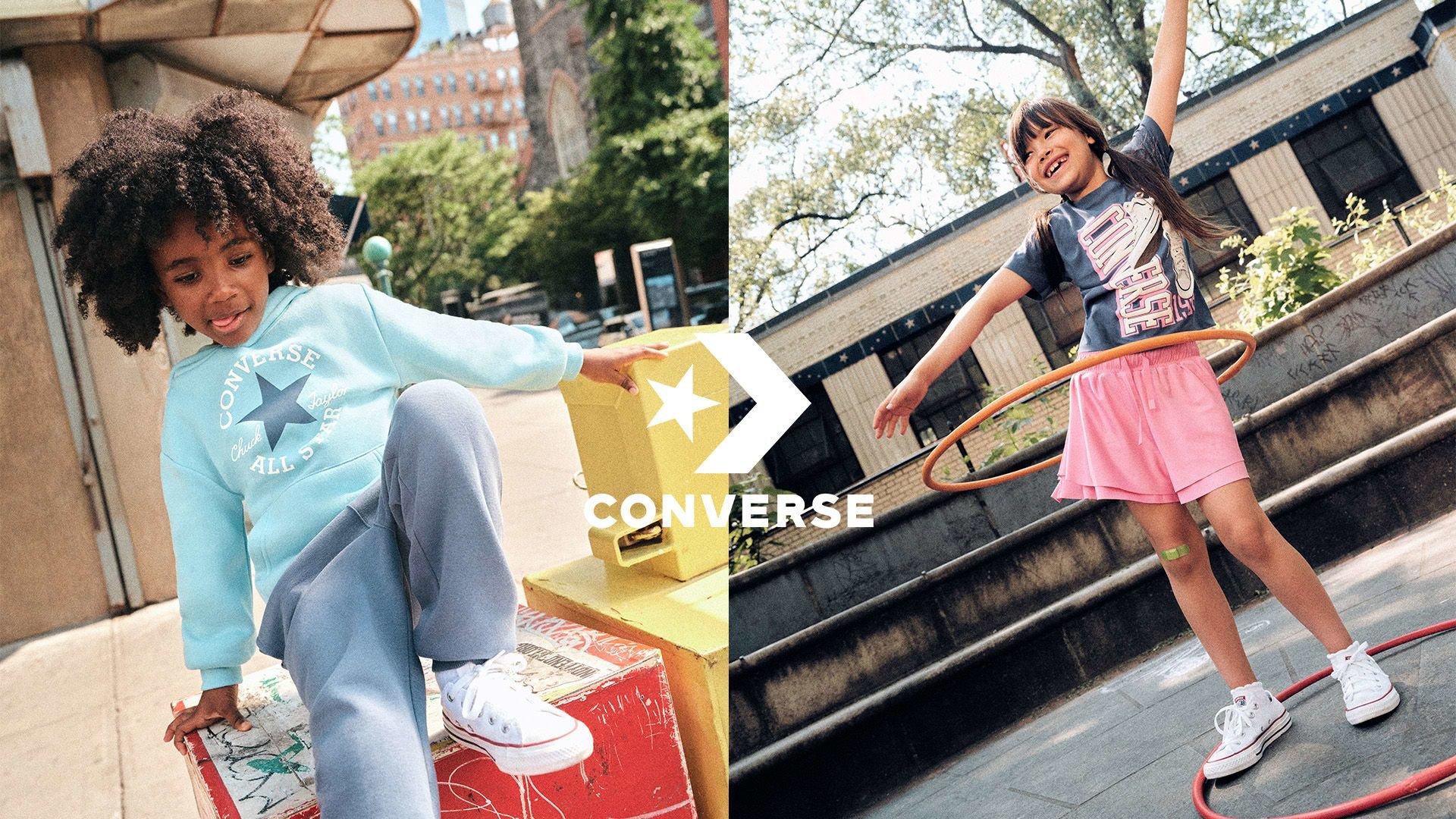 Due bambini in abbigliamento casual con scarpe Converse. Uno indossa un hoodie azzurro chiaro e pantaloni grigi, l'altro ha una maglietta scura e pantaloni corti rosa.