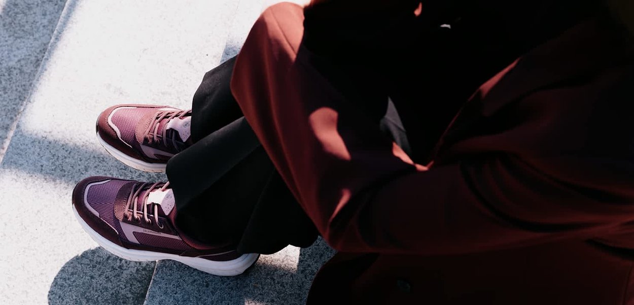 Purple athletic shoes with a textured upper, featuring white accents and laces, placed on a stone surface with partial leg visibility.