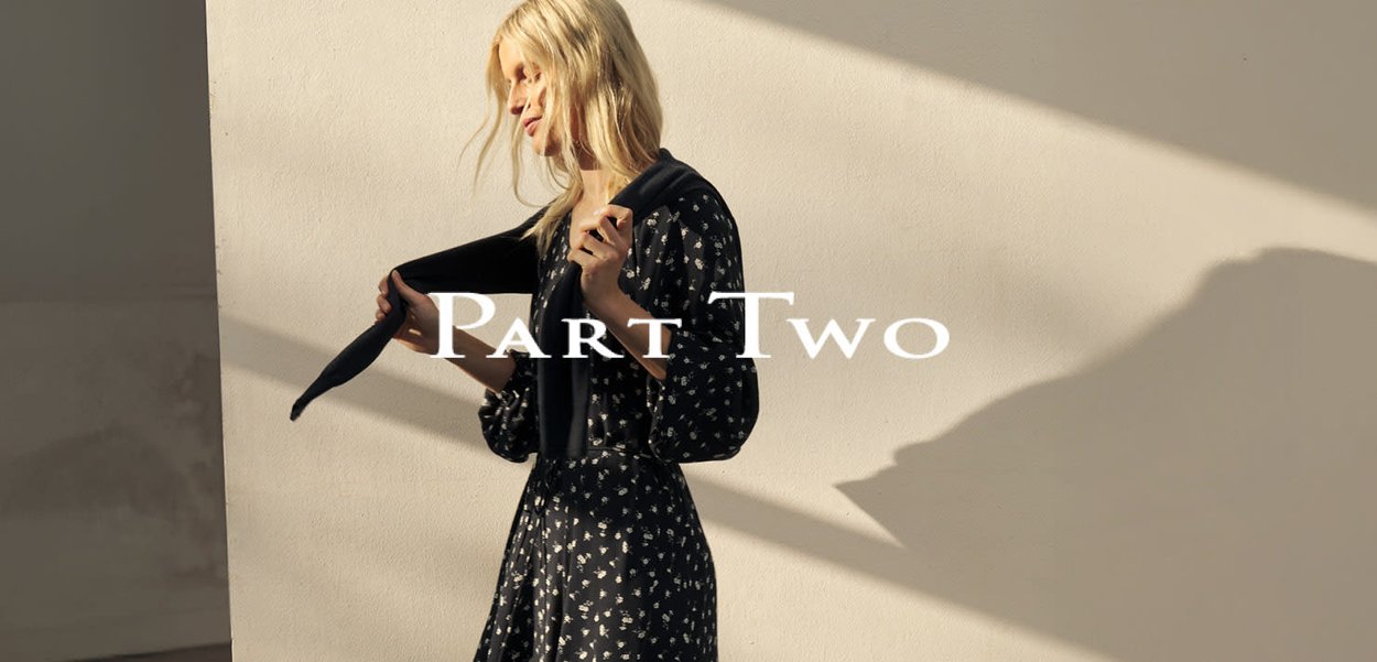 Schwarzes Kleid mit weißem Blumenmuster, legerer Schnitt und Puffärmel. Ein marineblauer Pullover ist über eine Schulter gelegt. Weiches Licht betont die Textur.