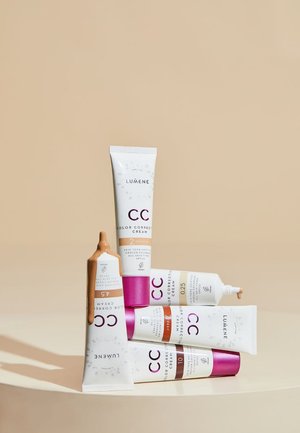Fem rør med Lumene CC fargekorrigerende krem arrangert på en flate. Rørene har hvite, beige og brune farger med rosa aksenter og etiketter.