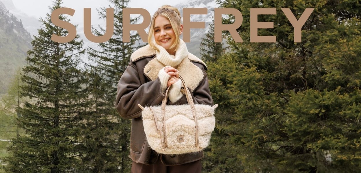 Wool-textured beige handbag with two short straps, featuring a central seam design and a logo plaque on the front, held by a person in a brown coat.