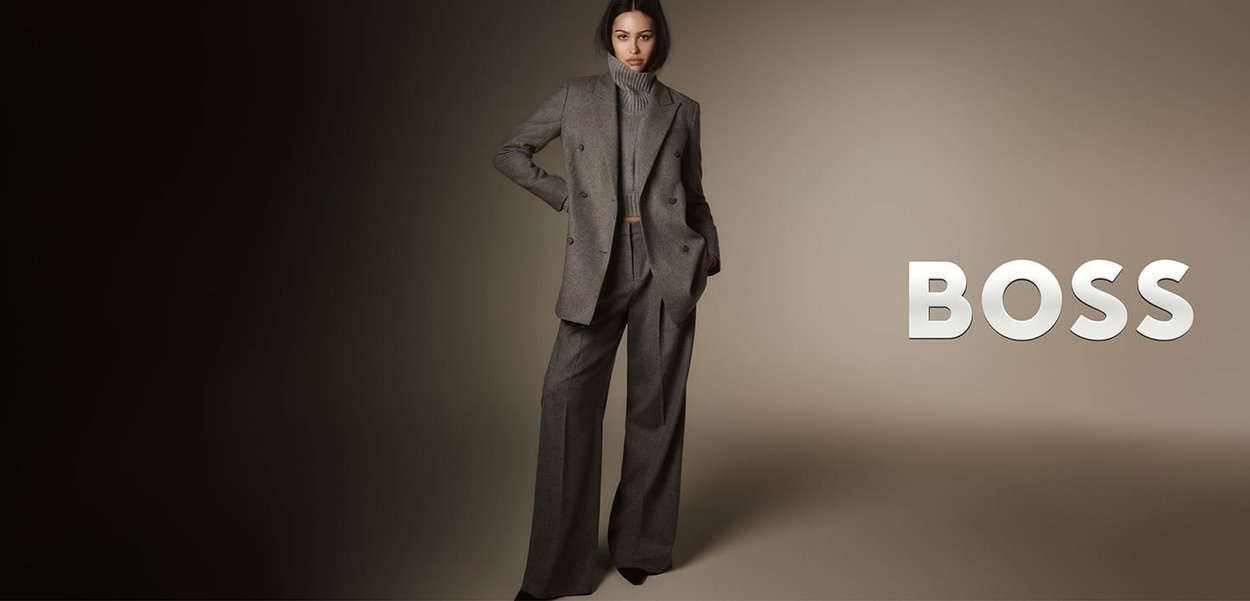 Completo grigio su misura con giacca doppiopetto e pantaloni a gamba larga, abbinato a un maglione a collo alto coordinato, indossato da un modello.