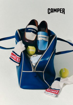 Mocasines de cuero azul y blanco dentro de un bolso de cuero azul abierto, con calcetines blancos y pelotas de tenis con la marca "Camper".