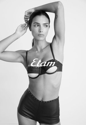 Bralette in finta pelle nera con aperture, dettagli borchiati e spalline regolabili abbinato a pantaloni corti a vita alta, anch'essi in finta pelle.