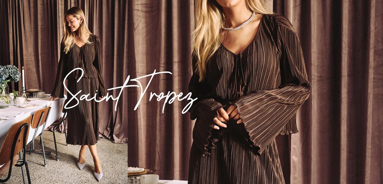 Braunes Faltenkleid mit langen Ärmeln, V-Ausschnitt und Bindeband-Detail, kombiniert mit funkelnden High Heels. Neutraler Hintergrund mit gedecktem Esstisch.