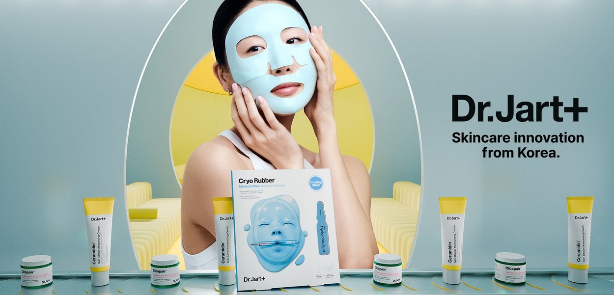 Dr.Jart+ Cryo Rubber moisturizing mask in blue packaging on a shelf, surrounded by skincare products in white and yellow tubes, with a model applying mask.