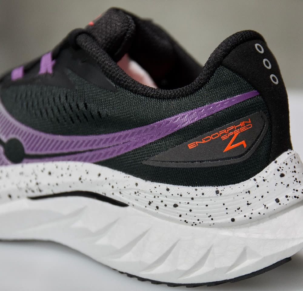 Schwarzer und lila Laufschuh mit strukturiertem Obermaterial, weißer Sohle mit schwarzen Sprenkeln und "ENDORPHIN SPEED"-Aufschrift in Orange.