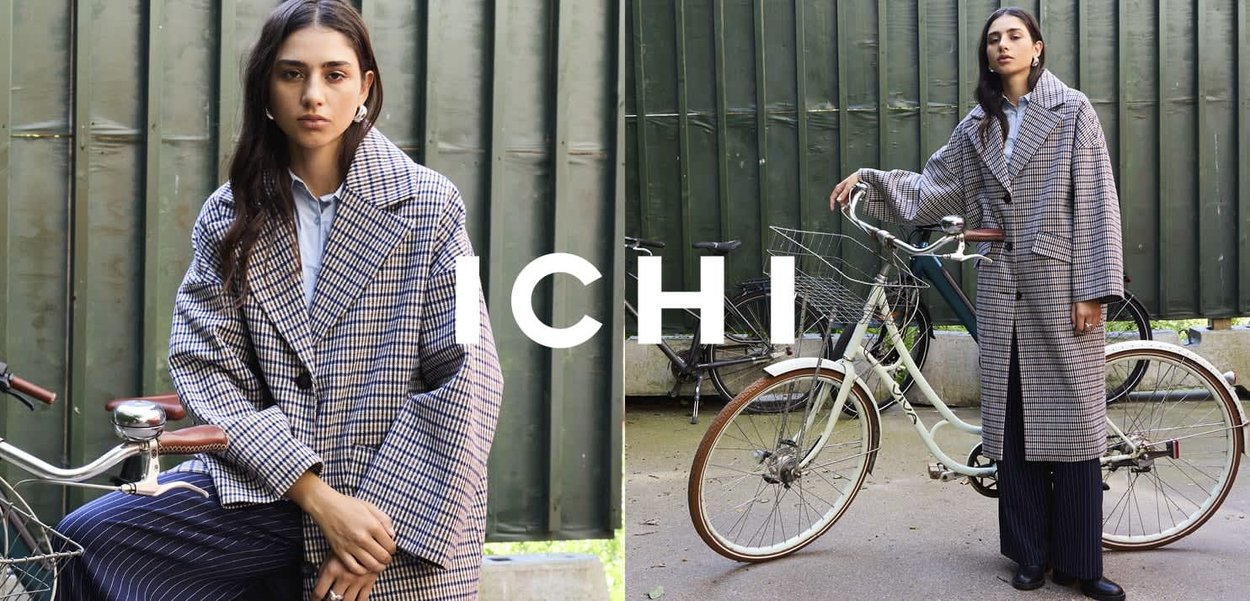 Checkered oversized coat in blue and white, featuring large lapels and pockets, paired with navy pinstripe pants. Bicycle in background.