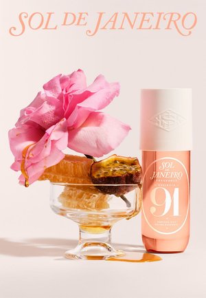 Flacon de parfum étiqueté "Sol de Janeiro 91" à côté d'un plat en verre contenant un rayon de miel, une moitié de fruit de la passion et une fleur rose dégoulinant de miel.