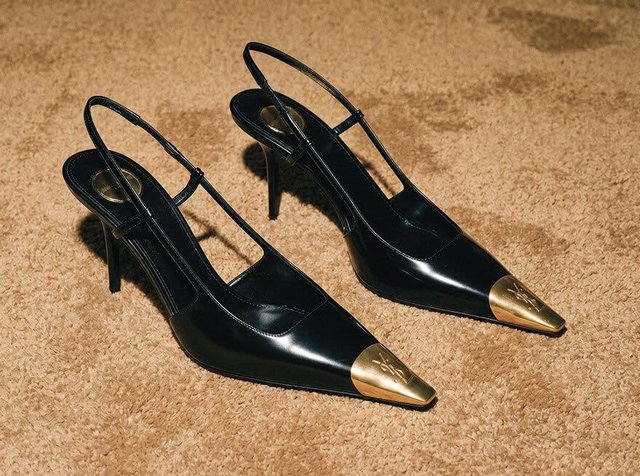 Escarpins slingback en cuir noir à talons hauts avec pointes métalliques dorées, posés sur un tapis beige.