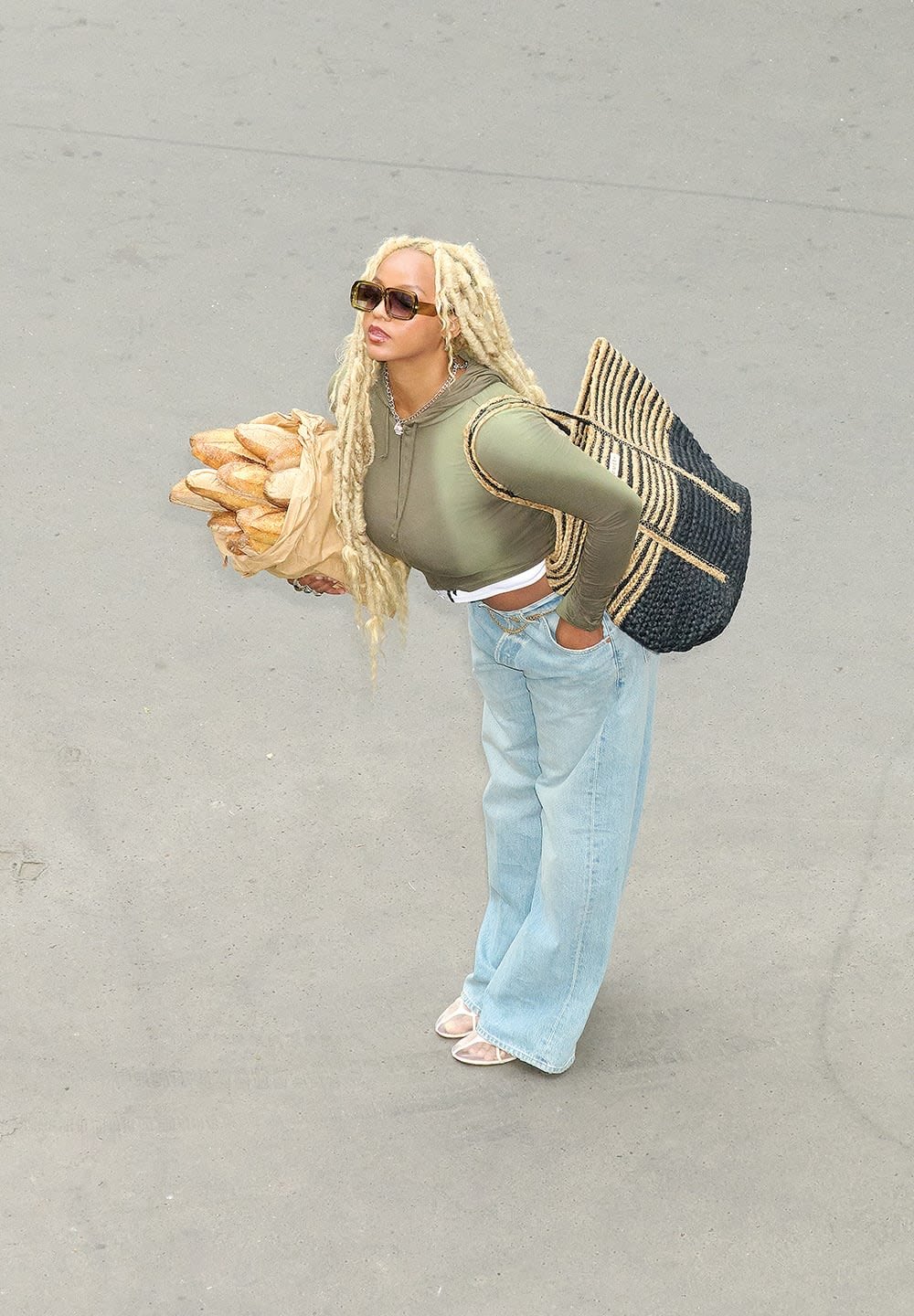 Groene lange mouwen crop top, lichtblauwe wijde jeans, een tas met baguettes, met een geweven zwarte draagtas en een zonnebril.