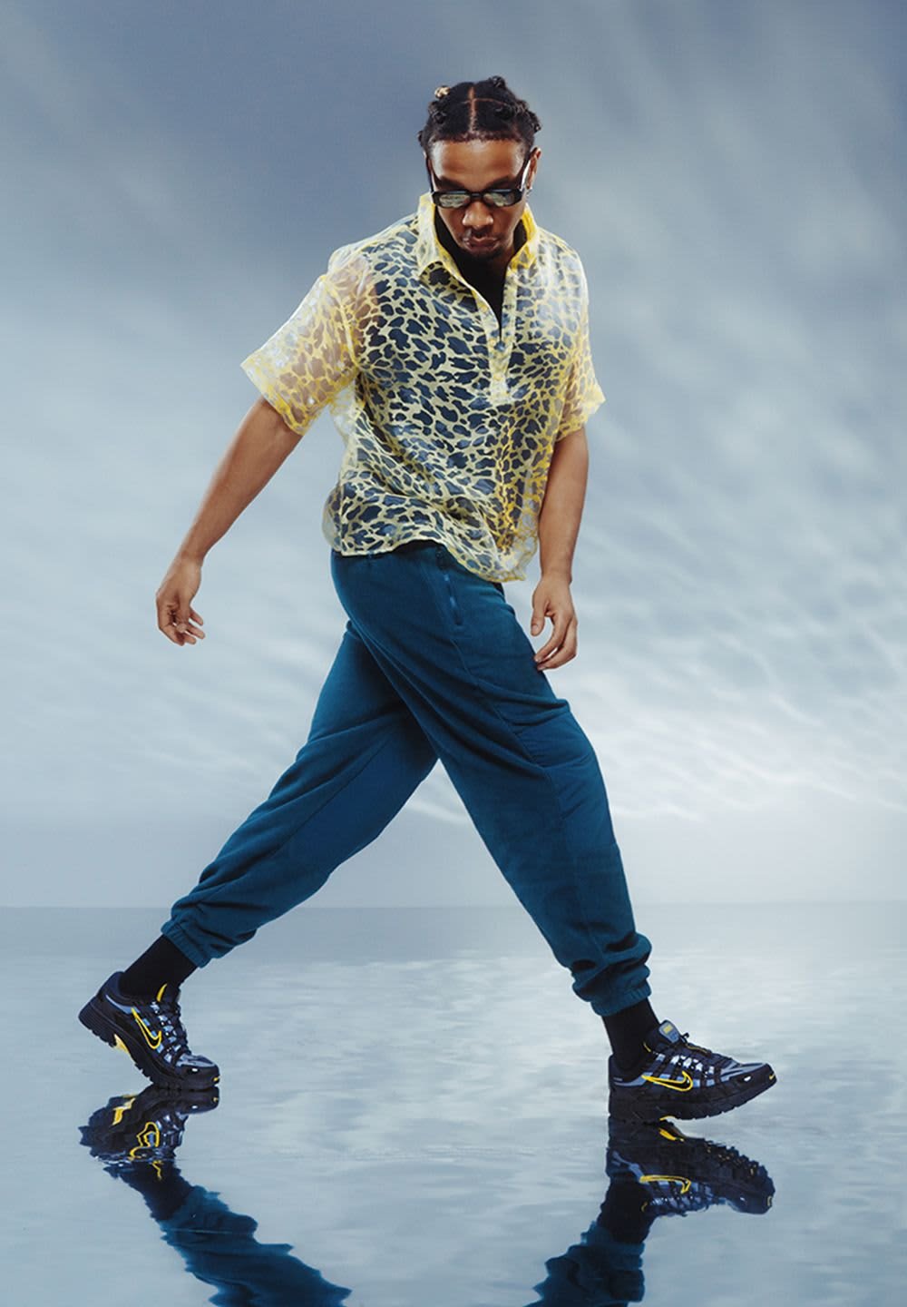 Yellow leopard print short-sleeve shirt, blue joggers, and black sneakers with yellow accents. Smooth surface and reflective background.