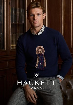 Maglione blu navy con un motivo lavorato a maglia testurizzato che presenta un cane in beige e rosso. Abbinato a pantaloni grigi a quadretti.