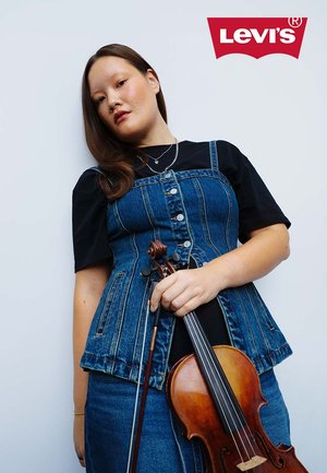 Gilet in denim Levi's con bottoni, indossato sopra una maglietta nera. La persona tiene un violino, con una finitura in legno naturale, su uno sfondo semplice.
