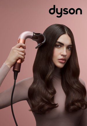 Strumento per acconciare i capelli Dyson con un design rosa e argento, caratterizzato da un manico curvo, una presa texturizzata e un lungo cavo di alimentazione, su uno sfondo rosa.