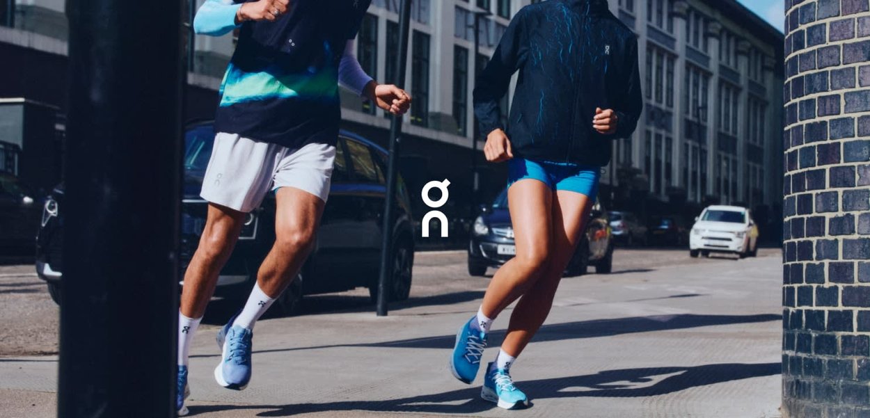 Two runners in an urban setting, wearing blue and black running gear, with light-colored shoes and visible branding on the apparel.