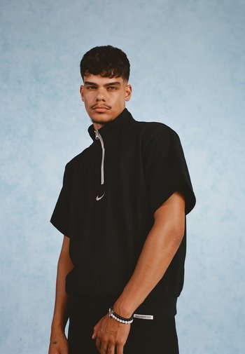 Zwarte met ritssluiting pullover met korte mouwen en een rechtopstaand kraag. Bevat een klein wit logo op de borst en een textuurstof.