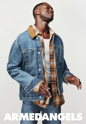 Jeansjacke mit einem braunen Cordkragen, über einem karierten Hemd getragen. Die Jacke hat zwei Fronttaschen und einen lässigen Schnitt.