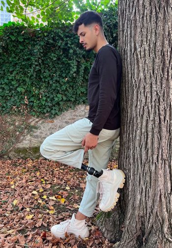 Vita hög-top sneakers med tjocka sulor, ljusgröna cargo-byxor och en svart långärmad tröja, lutad mot ett träd omgiven av höstlöv.