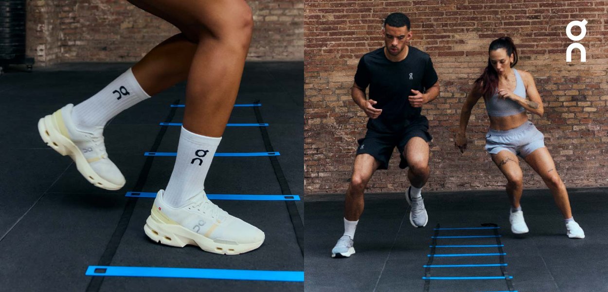 Dos personas realizan ejercicios de agilidad lateral en una escalera de entrenamiento azul en interiores, con un fondo de pared de ladrillo.