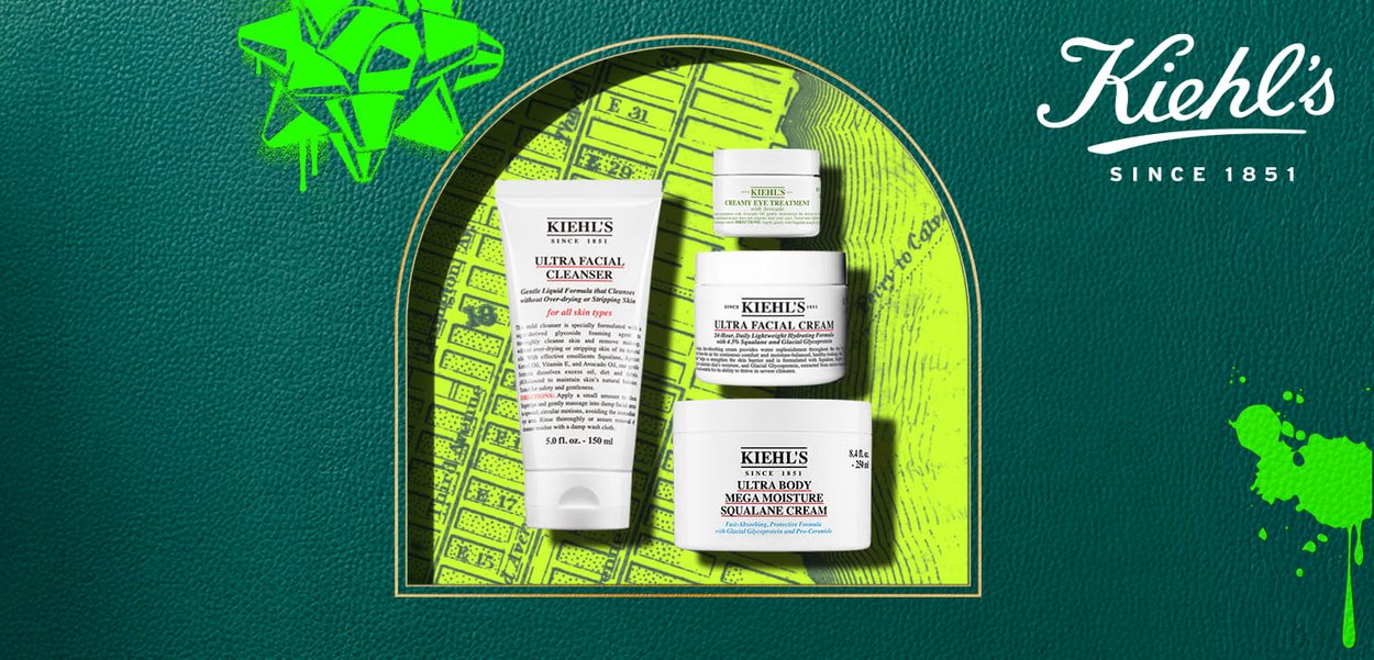 Four Kiehl's skincare products: a white cleanser tube, two white jars of cream, and a small eye treatment in a jar. All feature black text labels.