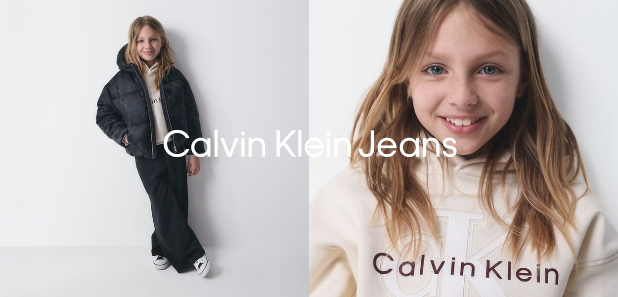 Veste en doudoune noire, sweat à capuche crème avec le logo 'Calvin Klein' en bourgogne, pantalon noir à jambes larges, et baskets blanches. Fond en bois clair.