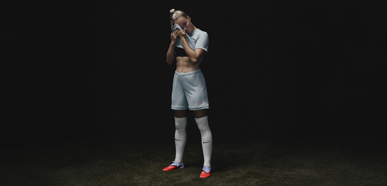Conjunto atlético de color azul claro que incluye una camiseta ajustada y pantalones cortos, combinado con calcetas blancas y botas de fútbol naranjas, sobre un fondo oscuro.