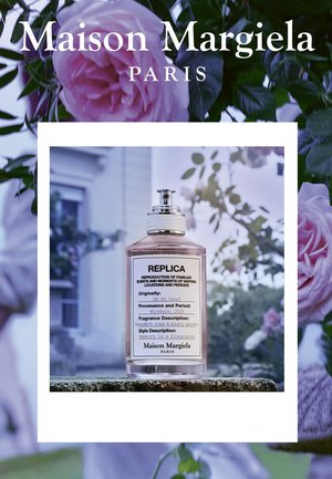 Maison Margiela Replica Parfümflasche mit Etikettendetails vor unscharfem floralen Hintergrund und Rosen, die die Szene einrahmen.
