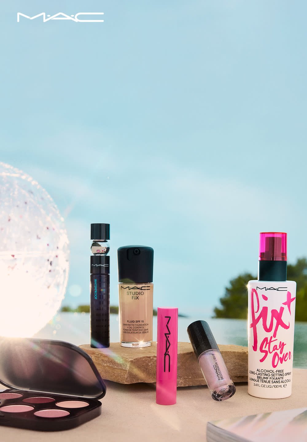 Prodotti cosmetici MAC disposti su una superficie: un mascara waterproof, una bottiglia di fondotinta, un prodotto labbra rosa e uno spray fissante, in diverse colorazioni.