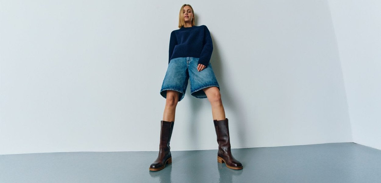 Brune læder knæhøje støvler med en blokhæl, parret med en navy-ribbet sweater og lyseblå denimshorts. Enkel design, minimale detaljer.