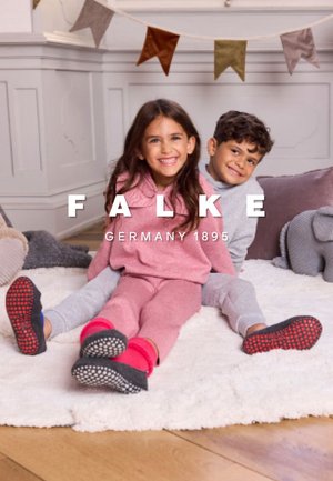 Two children sit on a plush white rug, wearing matching soft knit loungewear in light pink and gray, with colorful sock accents.