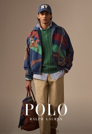 Veste bomber colorée avec des graphiques de chevaux, pull en maille torsadée verte, chemise à carreaux, pantalons beige et sac en cuir brun. Casquette bleue de New York accentue le look.
