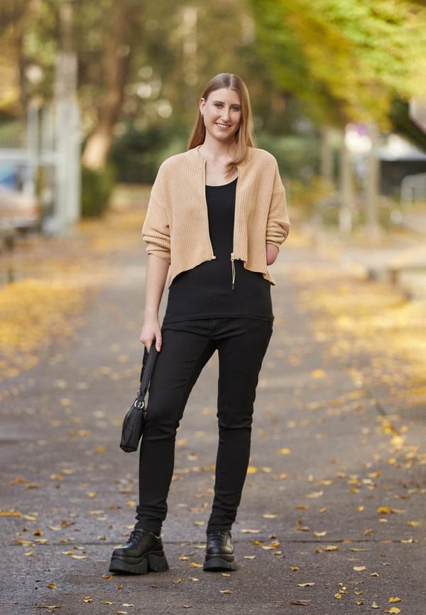 Beige stickad cardigan, svart topp och svarta åtsittande byxor. Kraftiga svarta plattformstövlar. Liten svart handväska. Utomhusmiljö med höstlöv.
