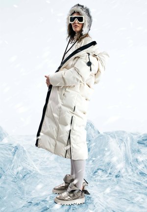 Puffer coat with a white exterior, black zippers, and a fur-lined hood, paired with metallic shoes and ribbed light-colored socks.