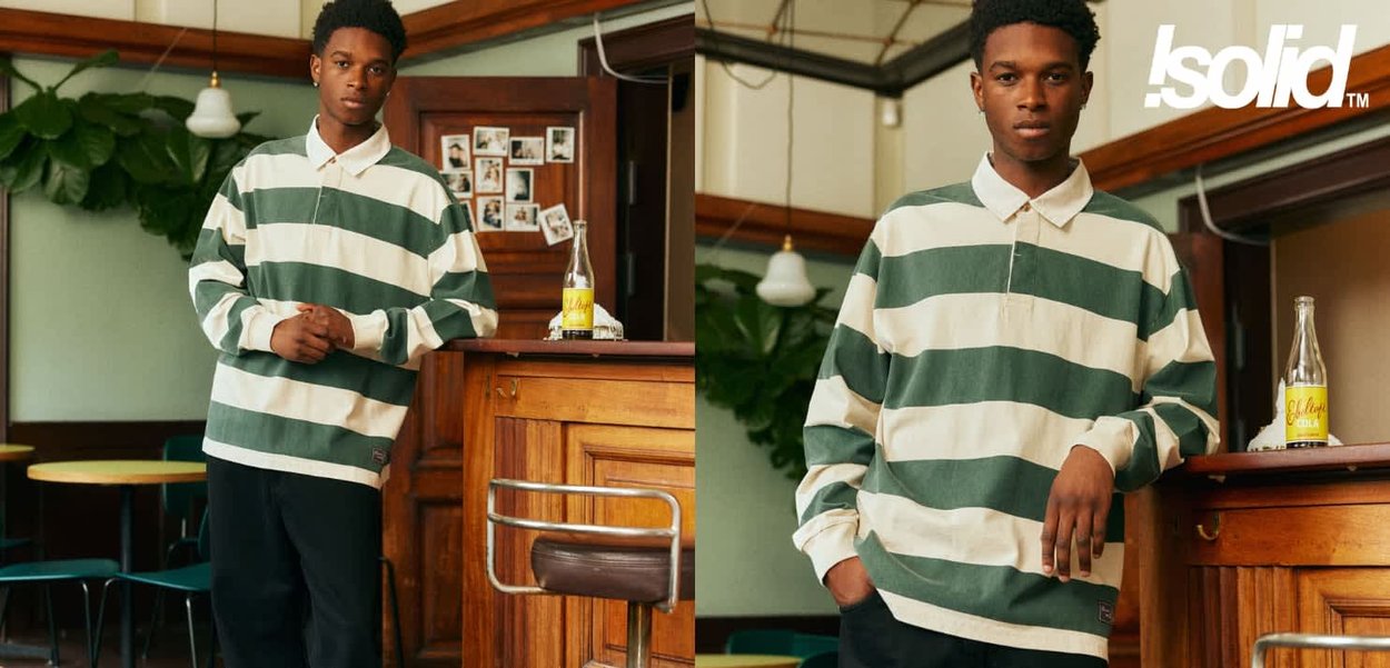 Grün-weiß gestreiftes langärmeliges Poloshirt aus Baumwolle mit Kragen und lockerem Schnitt, kombiniert mit schwarzen Hosen in einem Café-Ambiente.