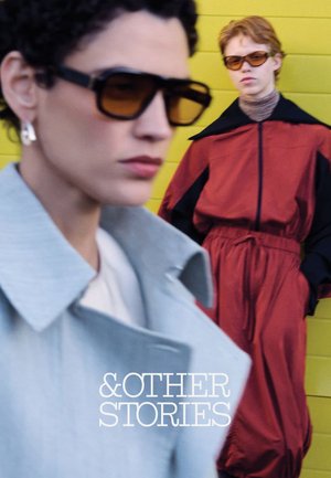 Two people wearing sunglasses and stylish coats, one in gray close-up, the other in red against a yellow background with "&OTHER STORIES" text.